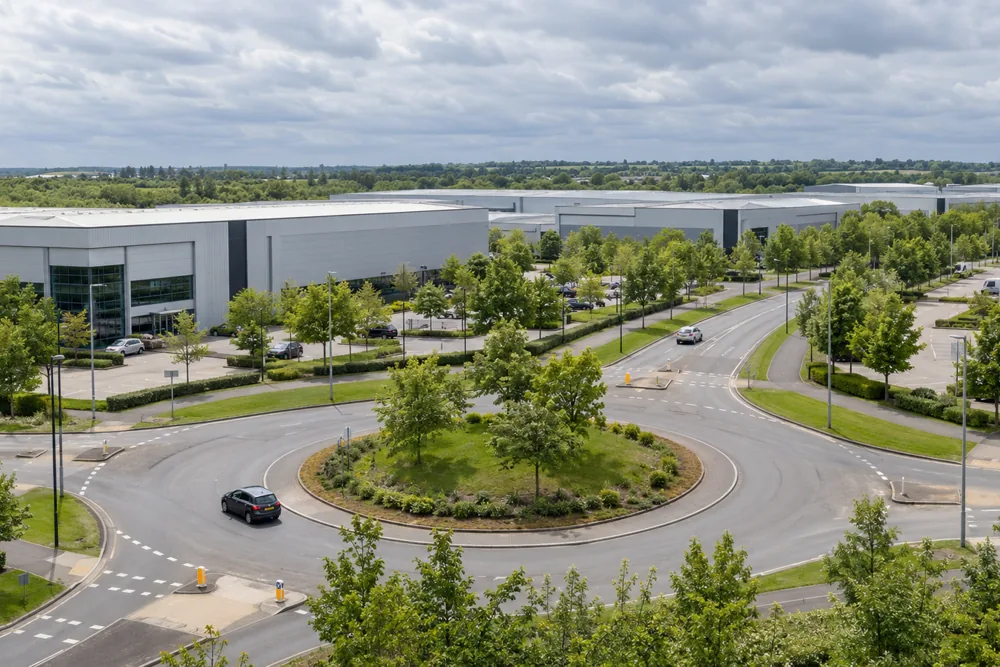 Tree-lined roundabout and roads beside modern warehouses in a Milton Keynes business park